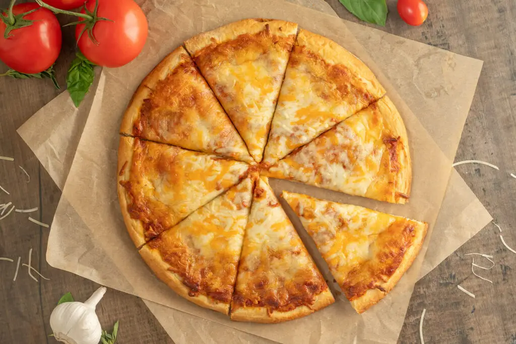 Top down photo of a baked Cheese pizza. The pizza is on brown parchment paper with ingredients scattered all around.