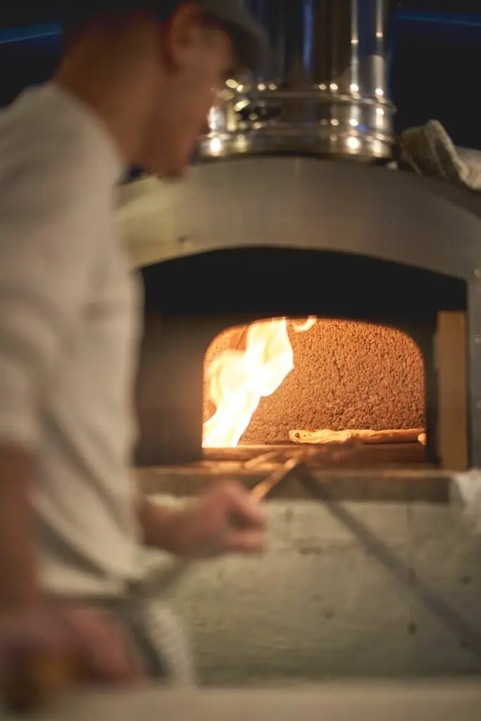 A chef using a wood fire oven to bake a pizza